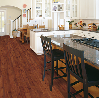 A spacious open-concept kitchen with rich, reddish-brown hardwood flooring, white cabinetry, and black-stooled kitchen islands