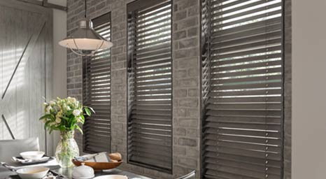 Dark wood horizontal blinds installed on windows over an exposed brick wall.