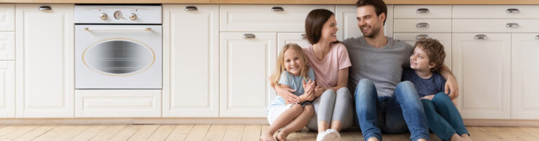 happy family sitting on wood plank flooring in kitchen hero - America's Carpet Barn